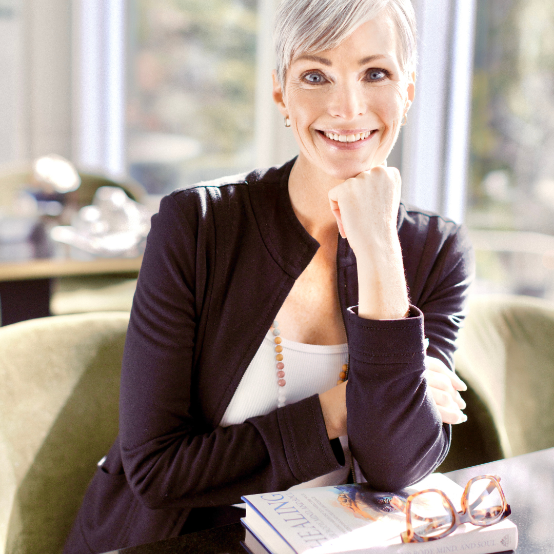 Brandi Garden sitting on a couch with a book and glasses, smiling.